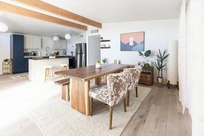 A modern kitchen with wooden cabinets, a stainless steel refrigerator, and a dining area with a wooden table and chairs. - Tucson Spring Escape | Stylish 3BR w/ Sunny Vibes (Tucson)
