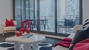 Una sala de estar moderna con un ventanal grande, un sofá blanco, un sillón rojo y una mesa de centro con un libro.