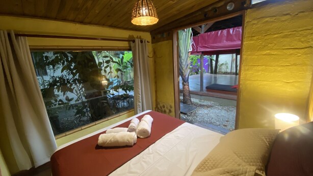 Quarto com cama, janela com cortinas, porta para o exterior e um abajur na parede.