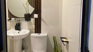 Een moderne badkamer met een wit wastafelmeubel, toilet en een grote spiegel boven het wastafelmeubel. Op de vloer staat een plant bij het toilet.
