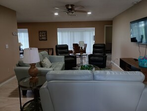 Una sala de estar con un sofá, dos sillones, una mesita de centro y un televisor montado en la pared.