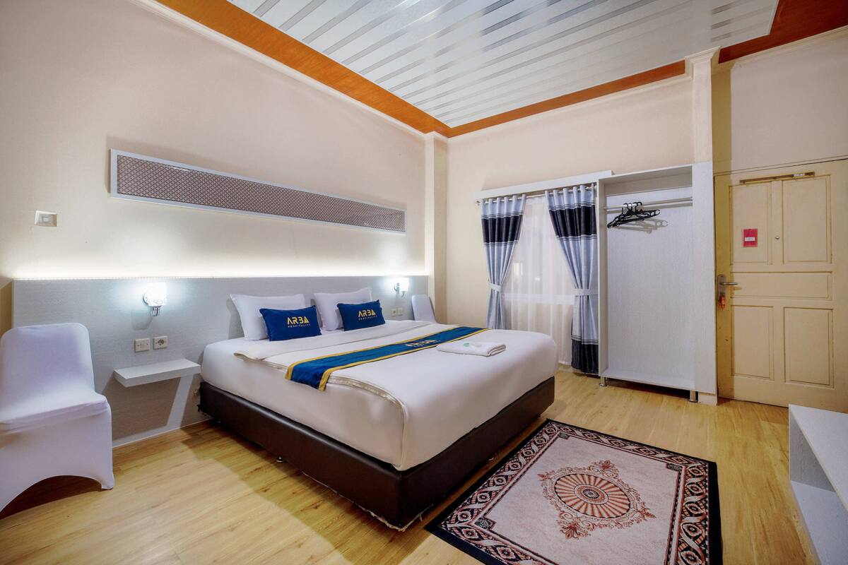 A hotel room with a bed, bedside tables, a chair, a wardrobe, and a patterned rug.