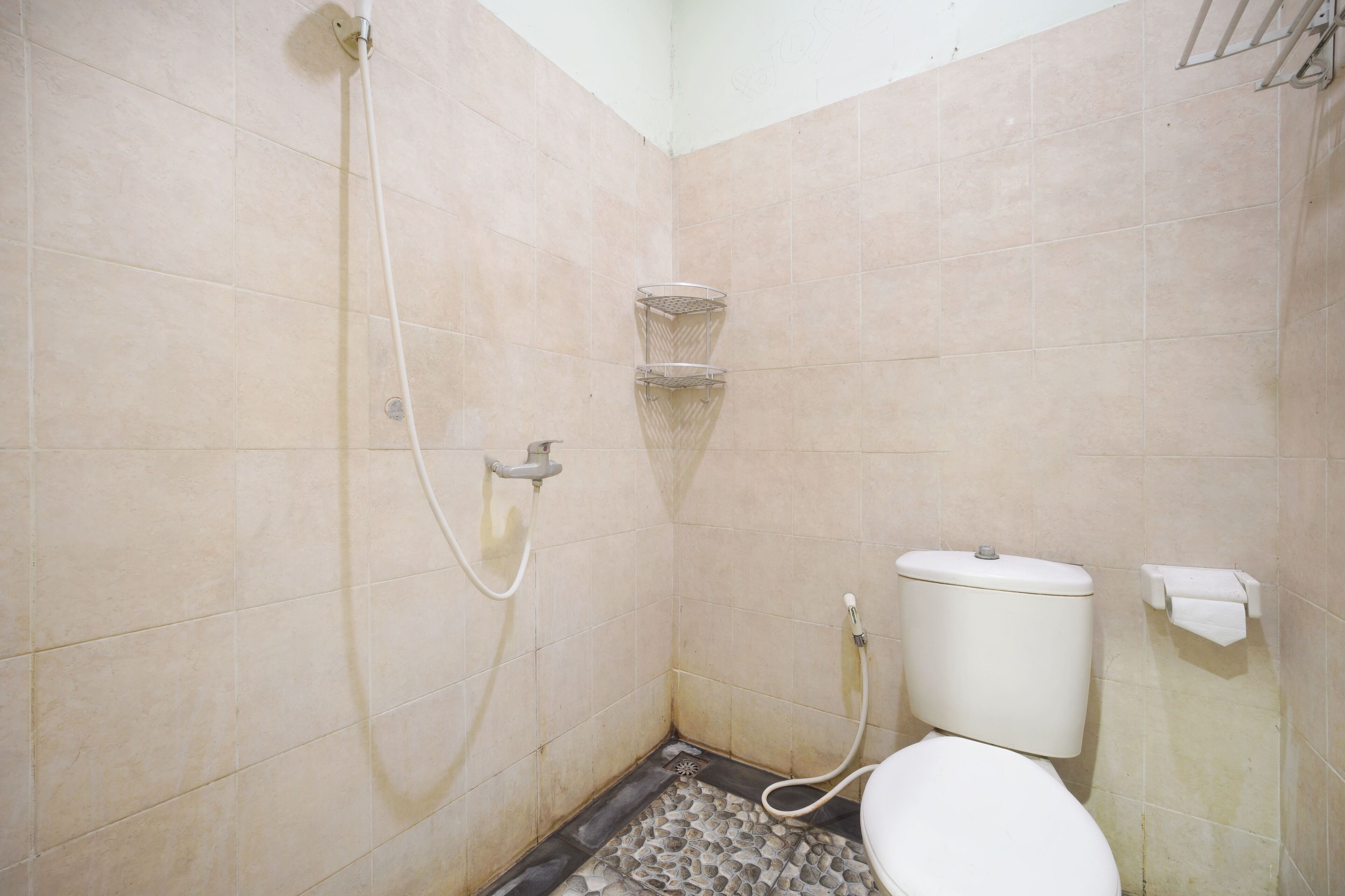 Een kleine badkamer met beige tegels, een toilet, een douche en een metalen plank.