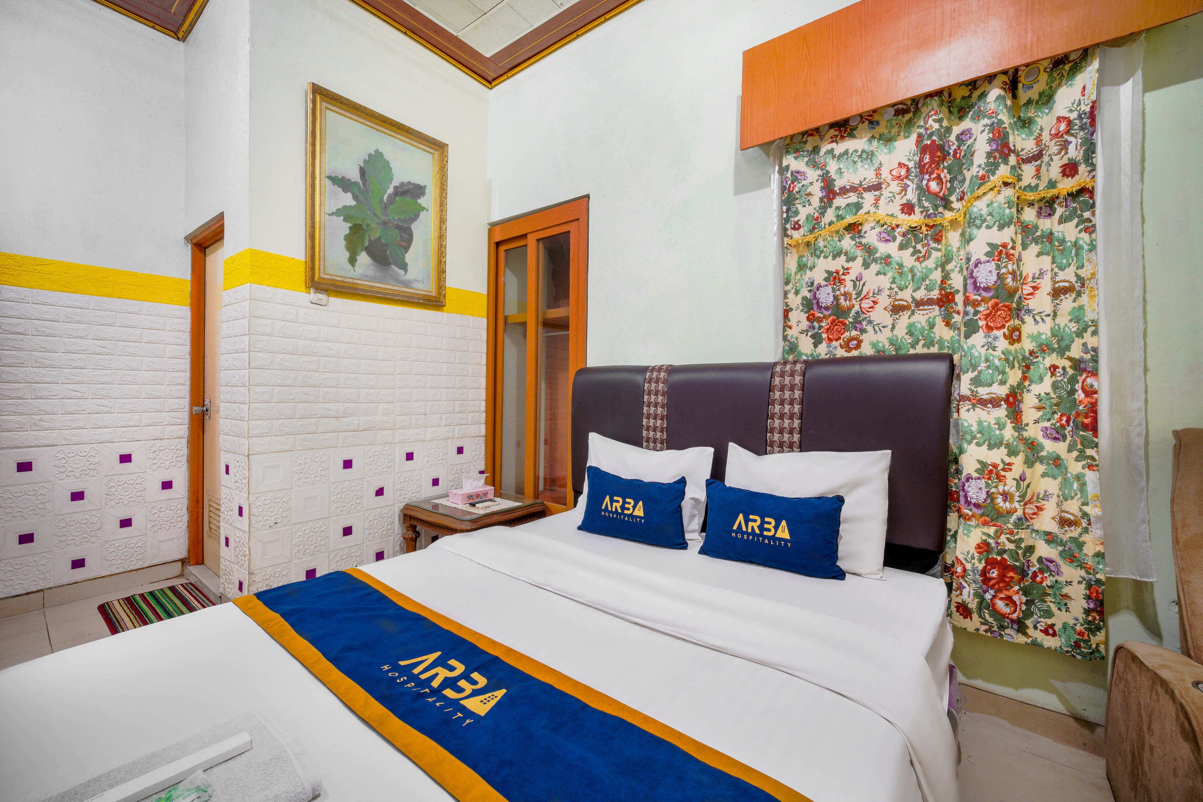 Una habitación de hotel con una cama, una mesita de noche, un espejo y una cortina estampada con motivos florales.