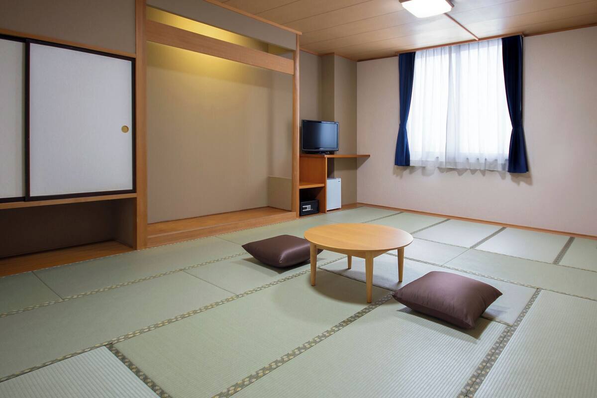 Una tradizionale stanza giapponese con pavimento in tatami, un tavolino basso, cuscini, un televisore e un armadio.