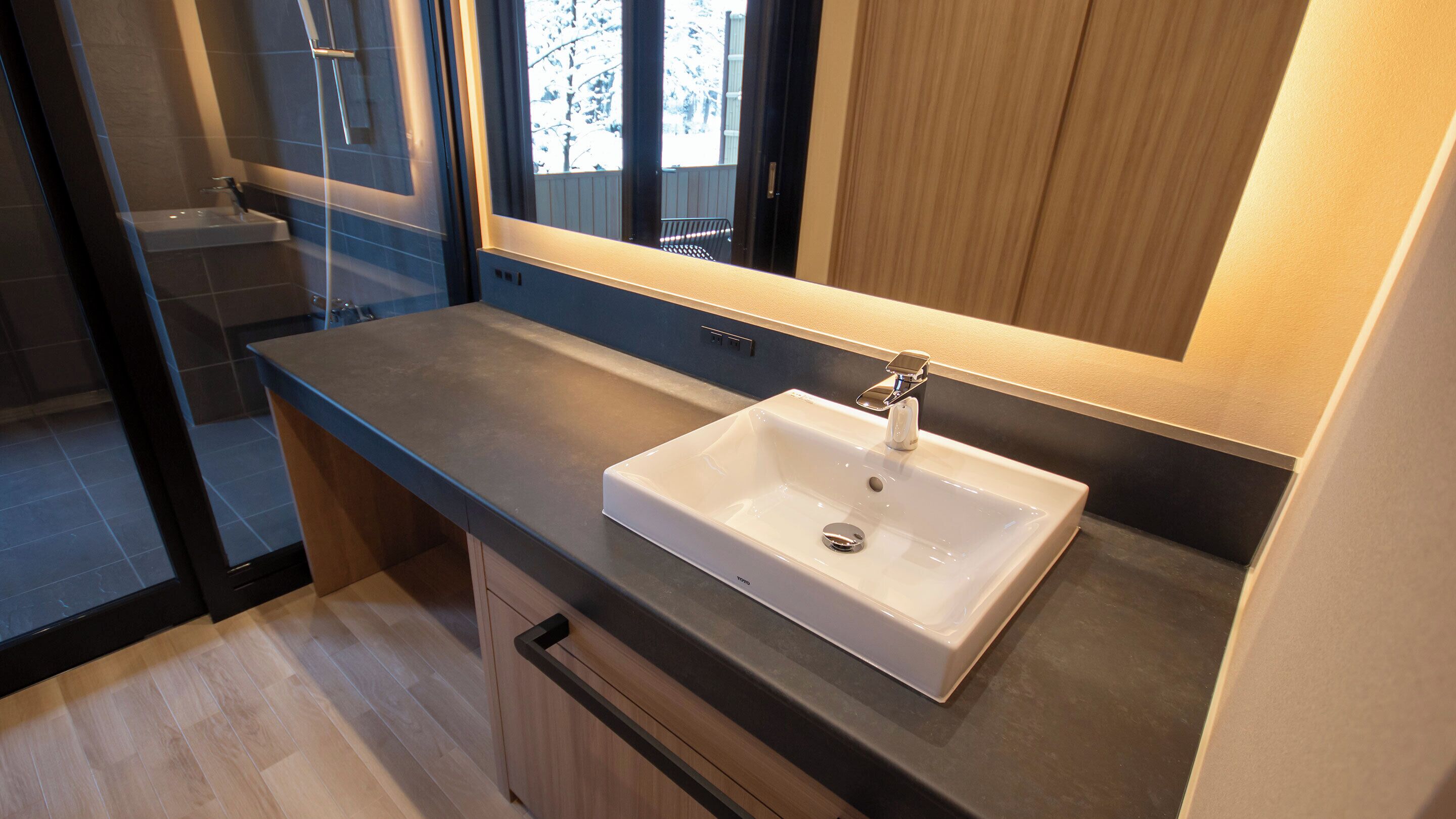 A modern bathroom with a white sink, a mirror, and a view of the outdoors.