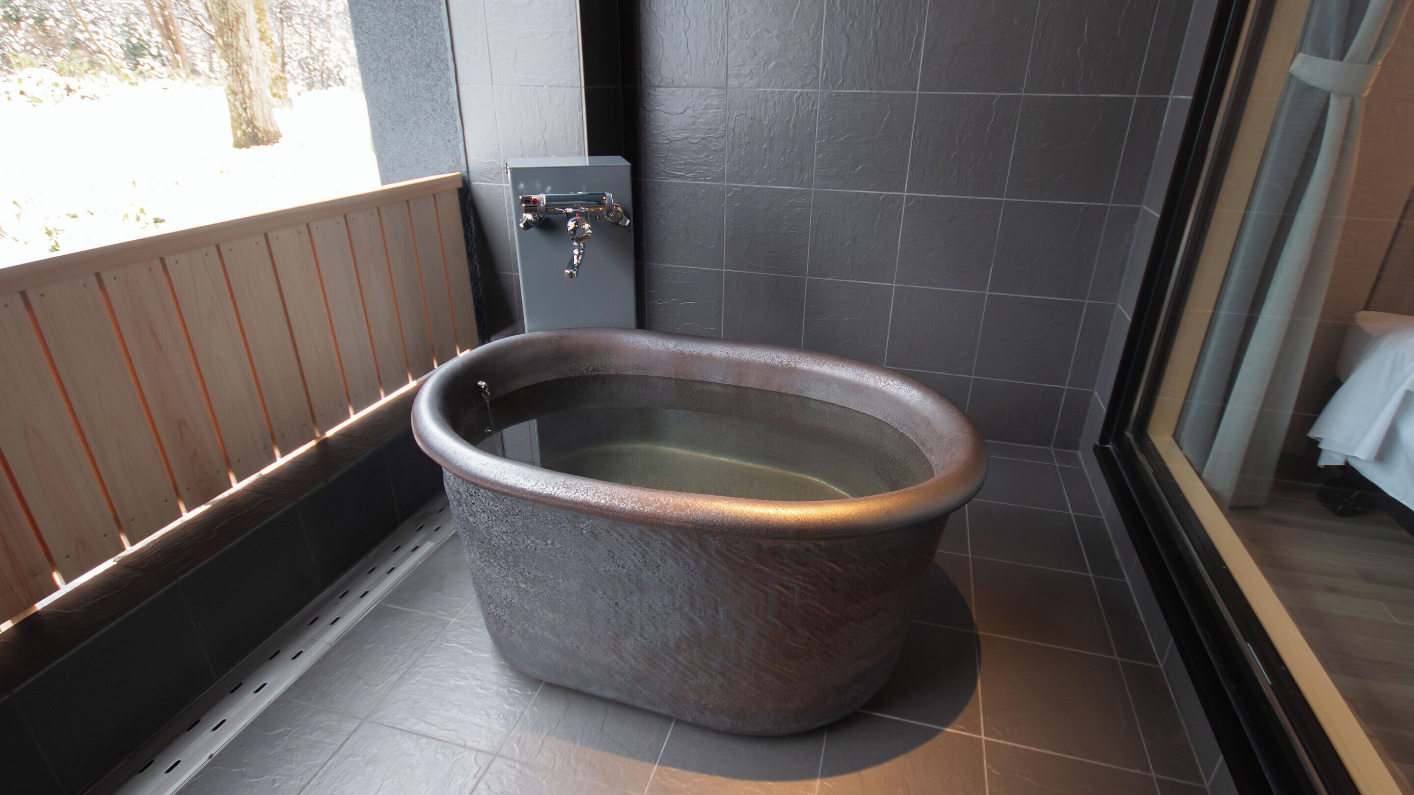 A modern bathroom with a large, round, stone bathtub, a wooden bench, and a control panel.