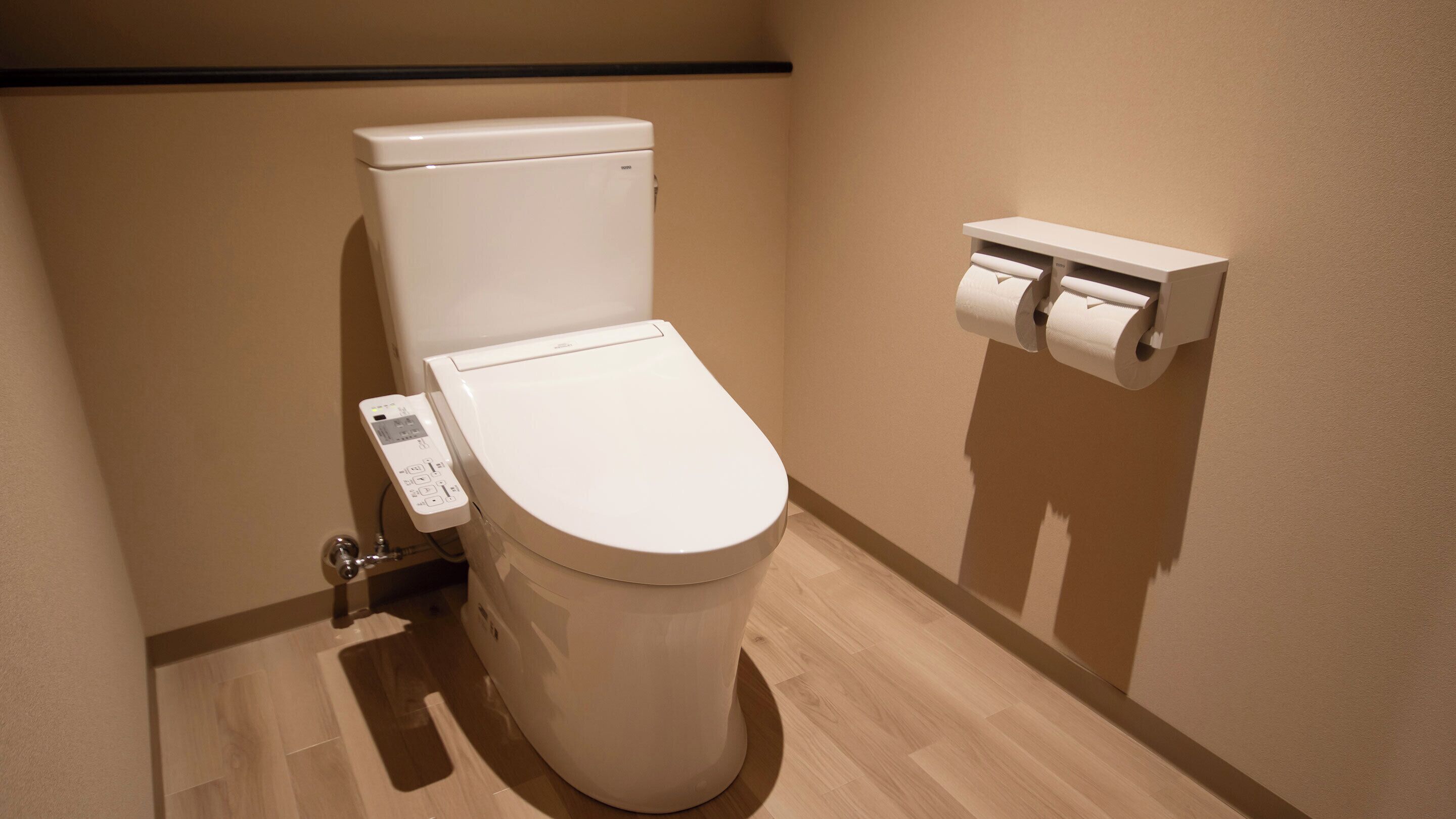 Un baño moderno con inodoro, dispensador de papel higiénico y panel de control.