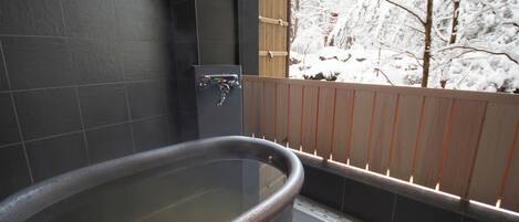 A bathtub in a room with dark tiled walls and a wooden fence outside.