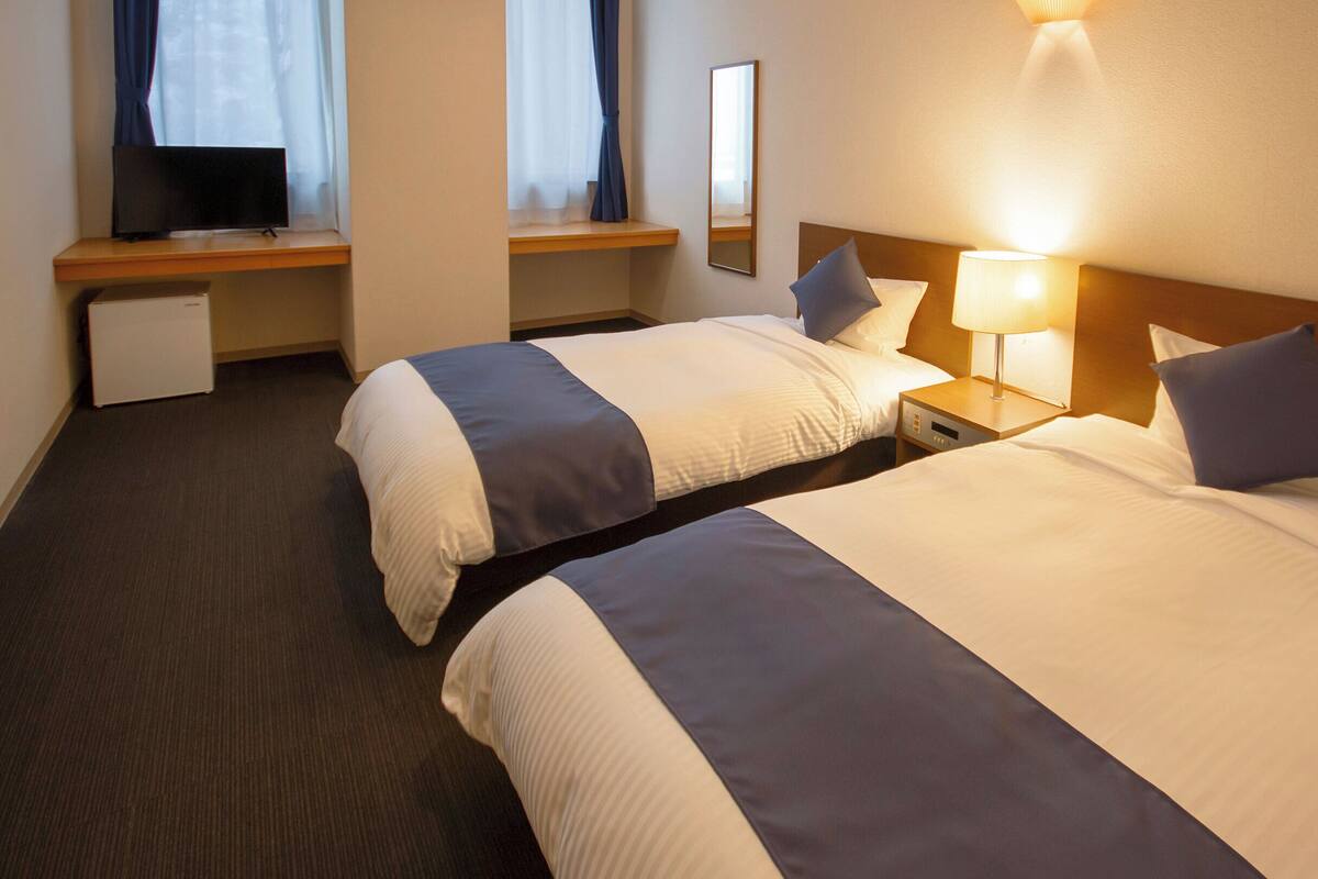 Una camera d'albergo con due letti, una scrivania, una televisione e una lampada da comodino.