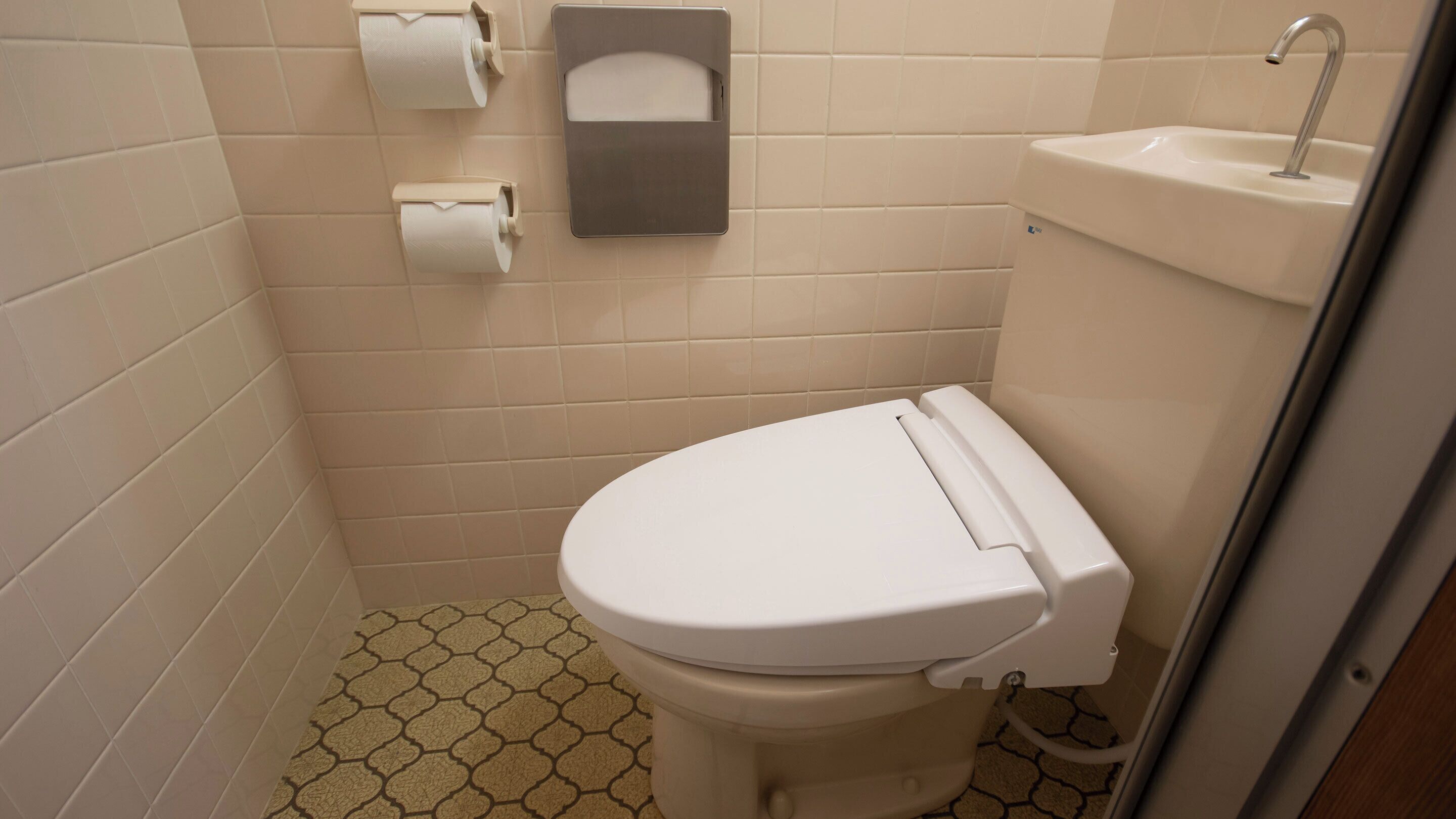 A small, clean bathroom with a toilet, a sink, and a paper towel dispenser.