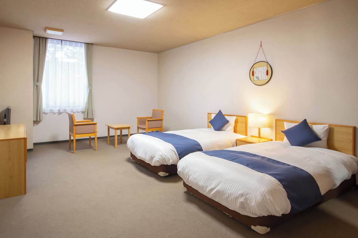 Camera d'albergo con due letti, una scrivania, una sedia, un tavolino e una finestra con tende.