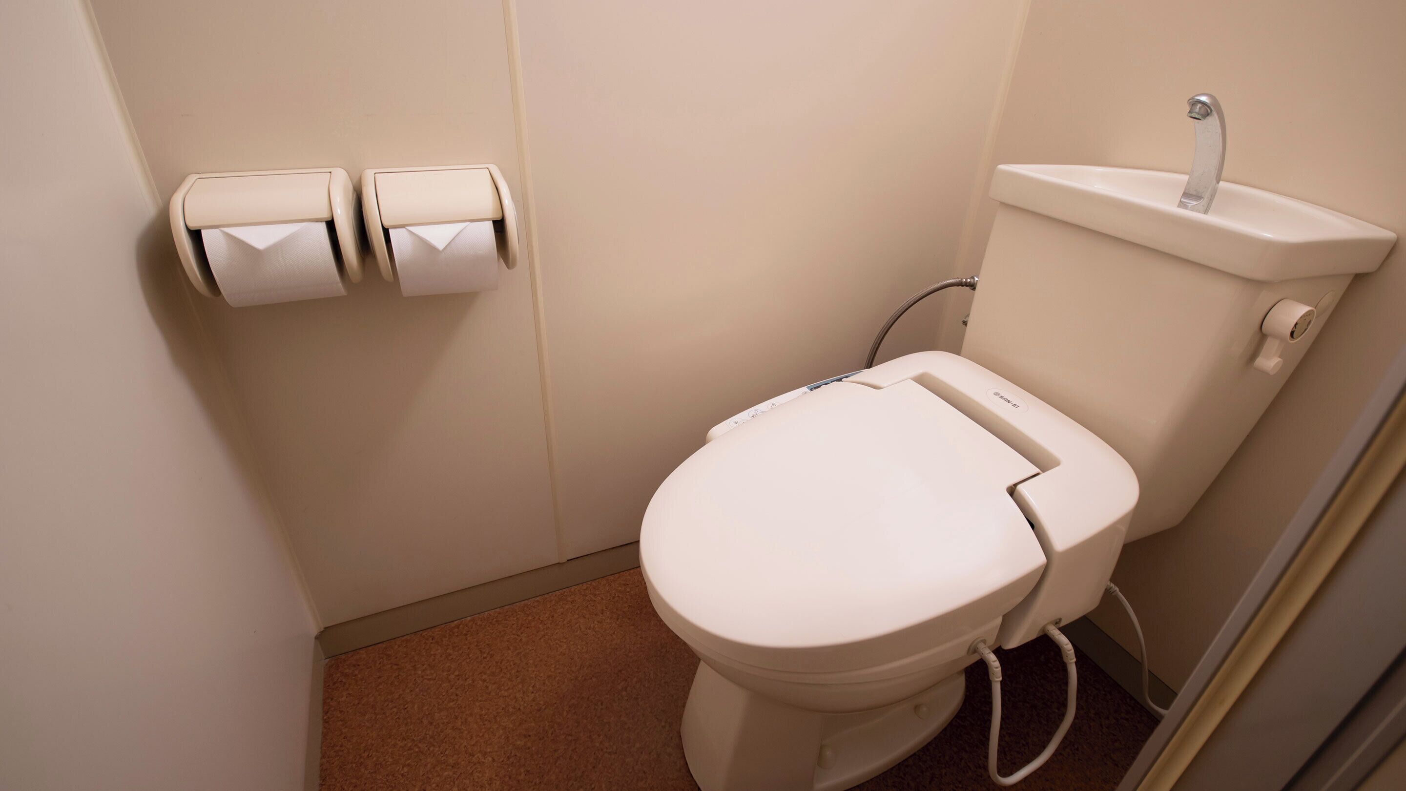 A small, compact bathroom with a white toilet, a sink, and two paper towel dispensers.