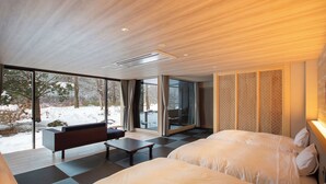 Een moderne hotelkamer met een grote schuifglazen deur naar een besneeuwde omgeving, een bank, een bed en een klein tafeltje.