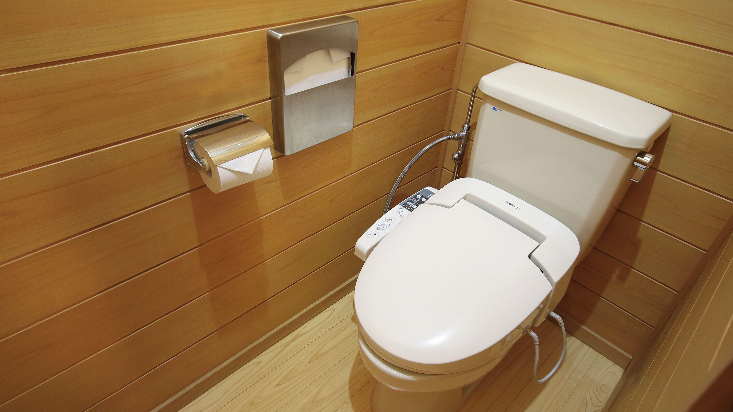 A modern bathroom with a wooden panel design, a toilet with a control panel, and a paper towel dispenser.