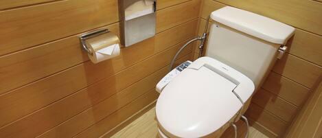 A modern bathroom with a wooden panel design, a toilet with a control panel, and a paper towel dispenser.