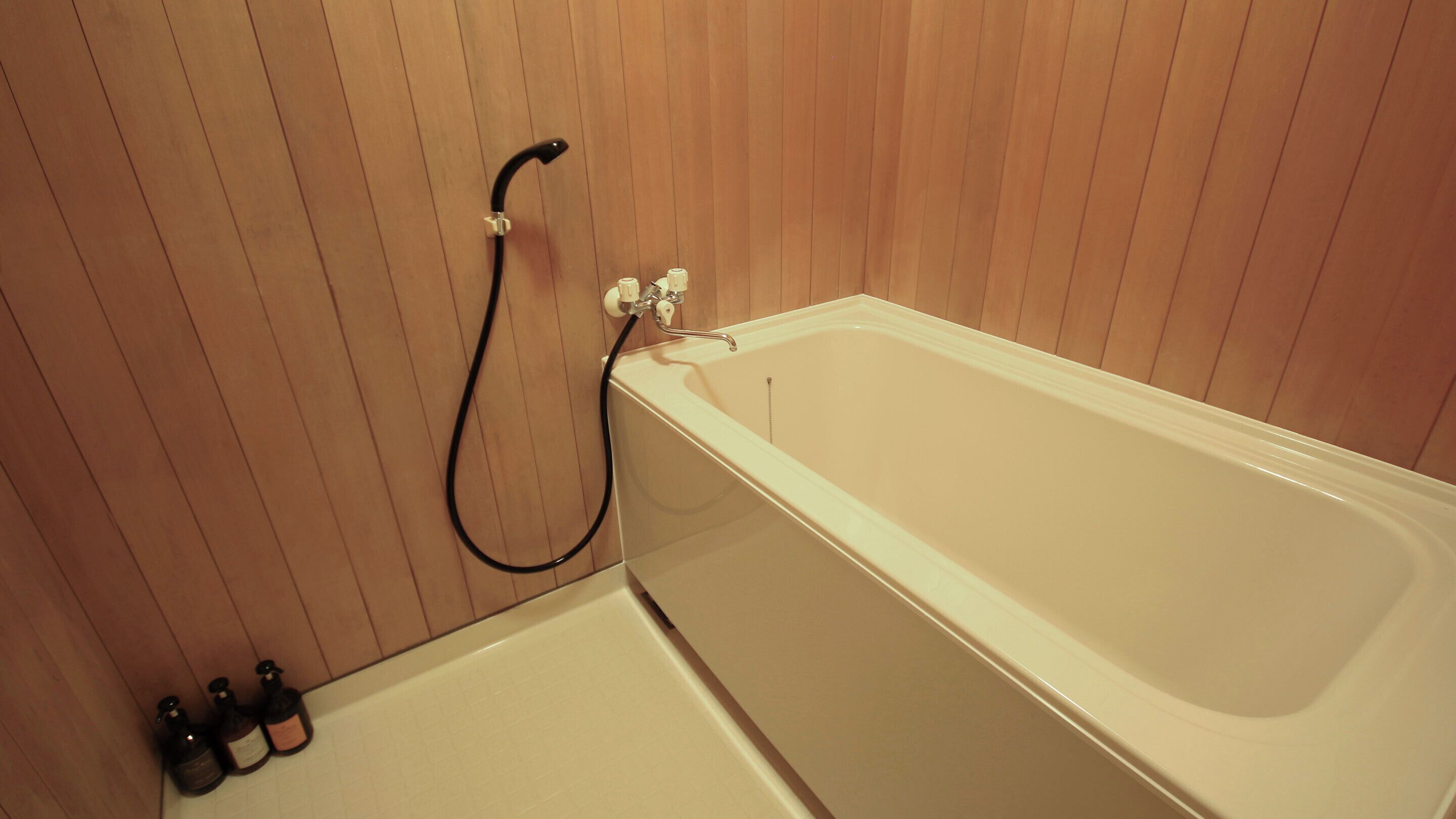 Un baño con una bañera blanca, paneles de madera y un cabezal de ducha de mano.