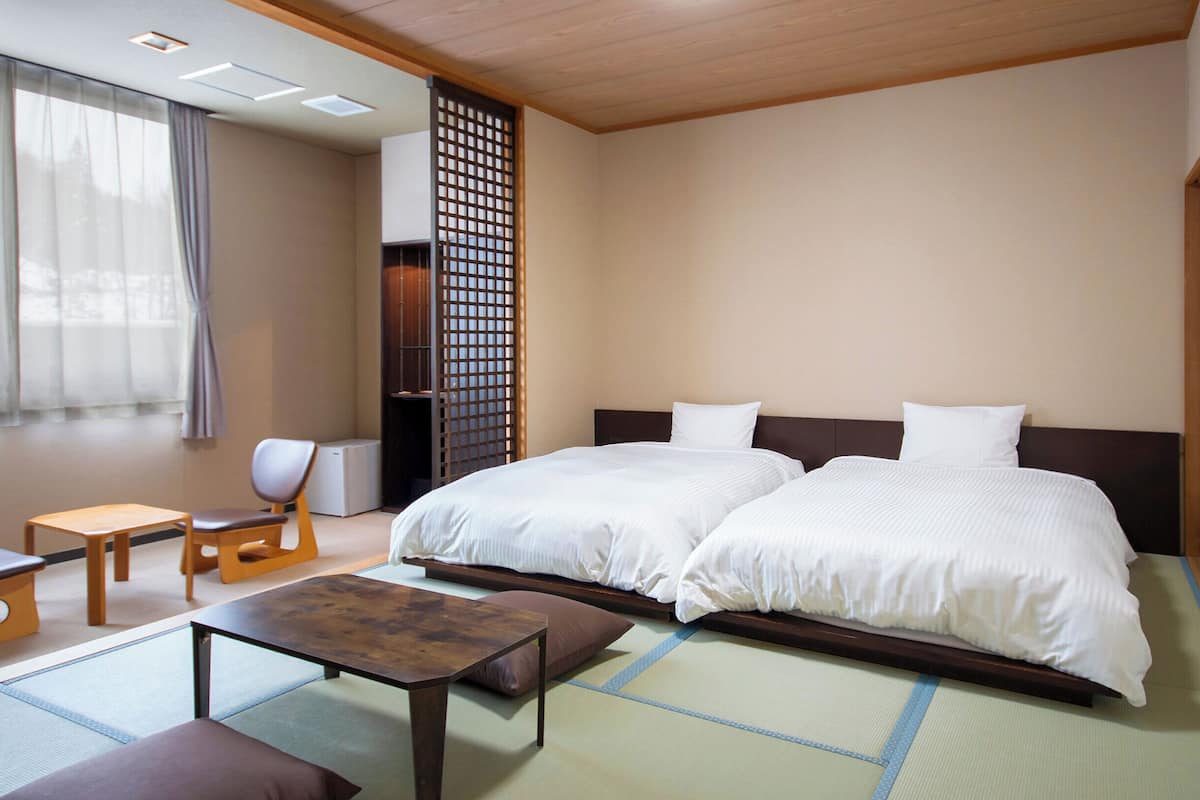 Una camera d'hotel con un'estetica tradizionale giapponese, caratterizzata da pavimento in tatami, pannello scorrevole shoji e un letto matrimoniale con biancheria da letto bianca.