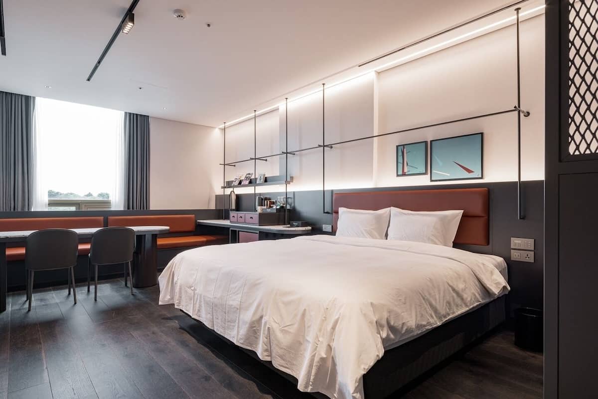 Habitación de hotel moderna con una cama grande, un escritorio con silla, ventana con cortinas y vistas al exterior.