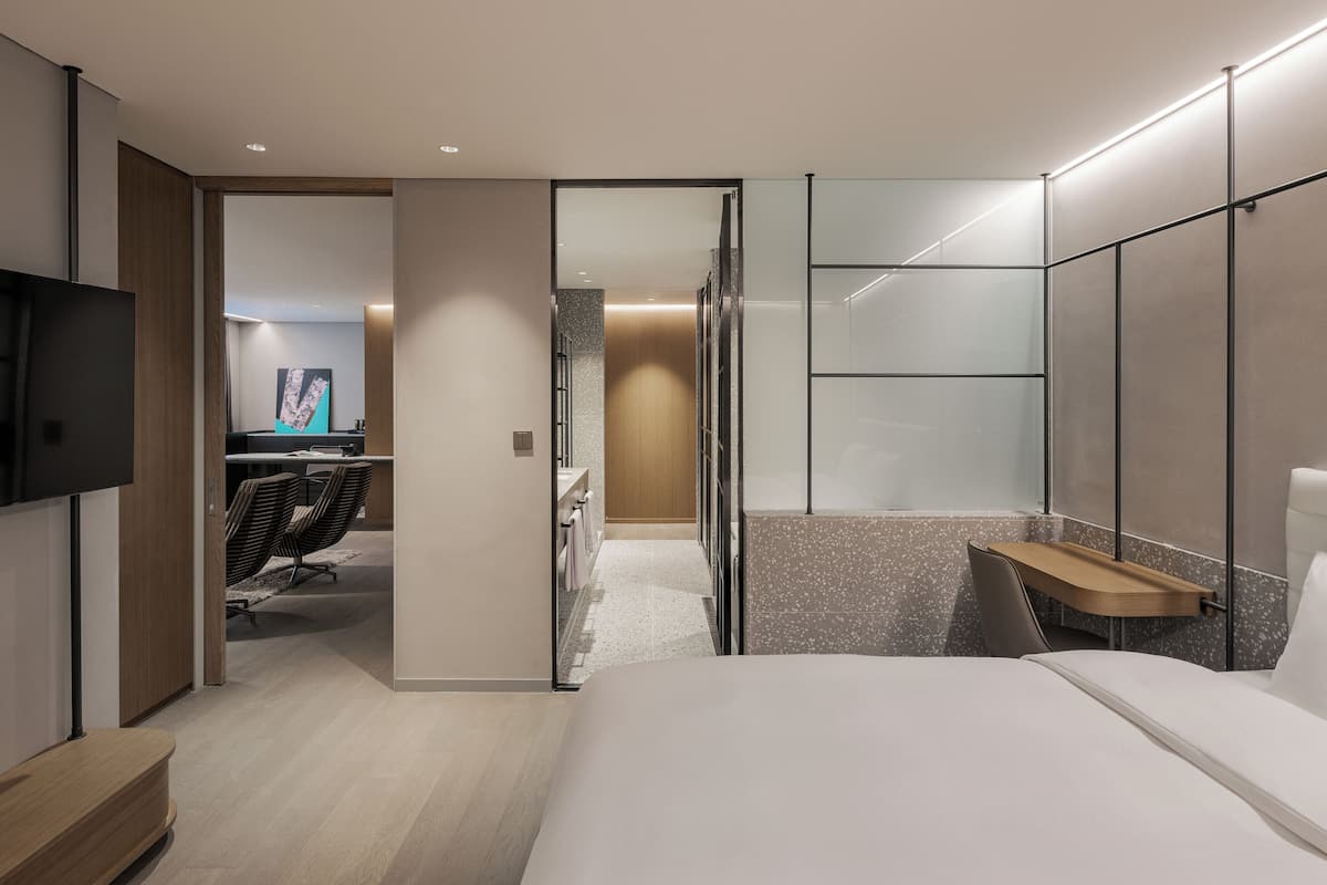 Una habitación de hotel moderna con cama, televisión, escritorio y zona de ducha.