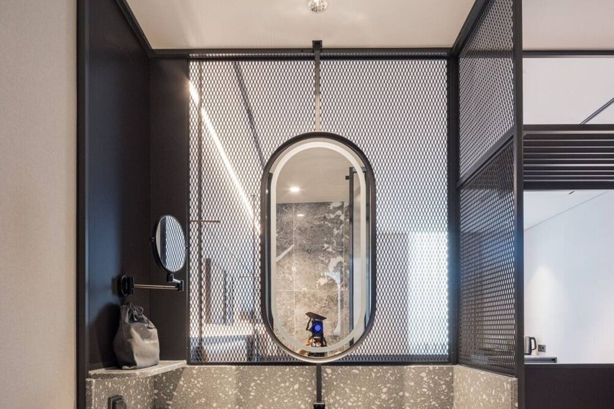 Un baño moderno con un espejo independiente, un lavabo con encimera moteada y dos toallas colgadas en un perchero.
