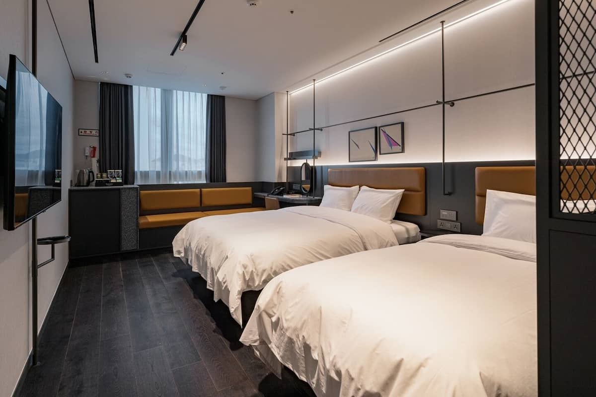 Habitación de hotel con dos camas, un escritorio, zona de estar y un ventanal grande.