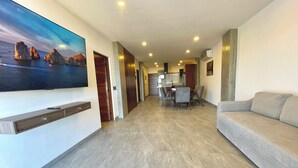 A spacious living area with a flat-screen TV mounted on the wall, a dining area with a table and chairs, and a sofa. - Marea Sabina Luxury Ocean View & Amenities (Cabo San Lucas)
