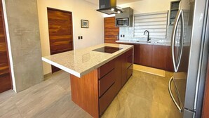 A modern kitchen with a granite countertop, wooden cabinets, a stainless steel refrigerator, and a microwave. - Marea Sabina Luxury Ocean View & Amenities (Cabo San Lucas)