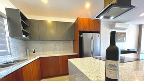 A modern kitchen with granite countertops, stainless steel appliances, and wooden cabinets. - Marea Sabina Luxury Ocean View & Amenities (Cabo San Lucas)