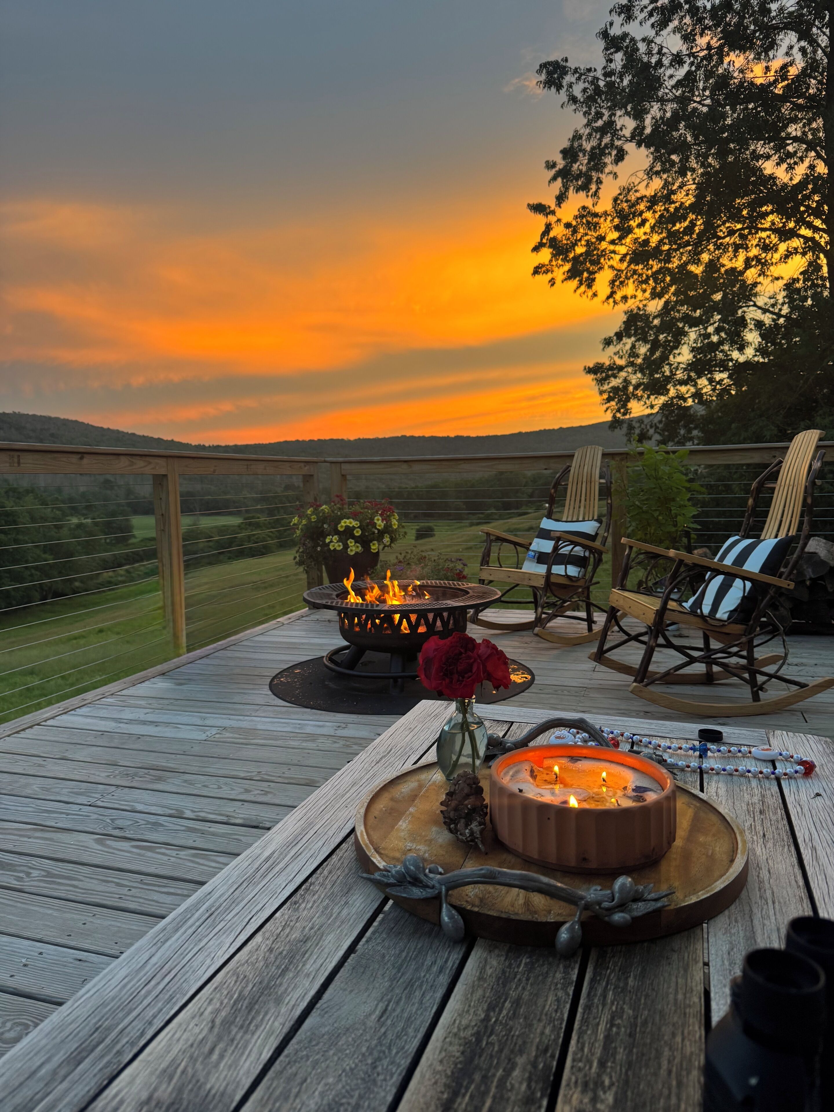 A deck with a fire pit, outdoor seating, and a scenic view during sunset.