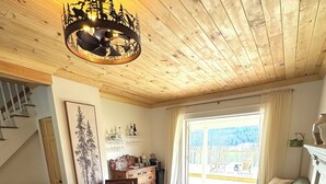 A cozy living room with a wooden ceiling, a chandelier, a sofa, a coffee table, and a view of a balcony. - NEW! Farmhouse Mountain View’s,FireplaceGrill, Pet-Friendly, Soaking Tub (Windham)