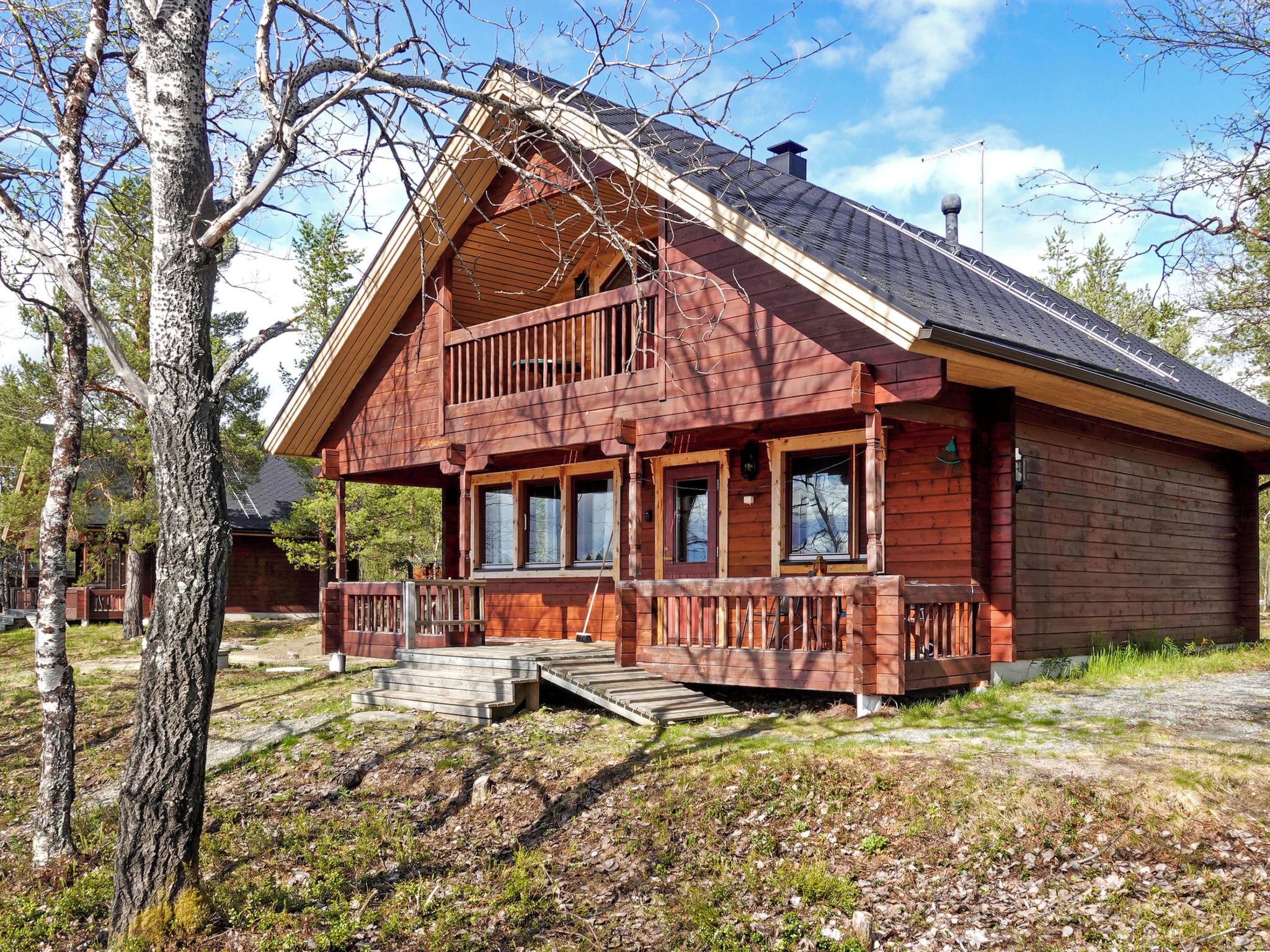 Een houten chalet met twee verdiepingen, een balkon, een veranda en een kleine trap naar de ingang.