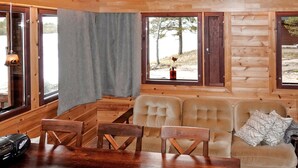 L’intérieur chaleureux d’un chalet avec une table à manger en bois, des sièges confortables et de grandes fenêtres offrant une vue sur l’extérieur.