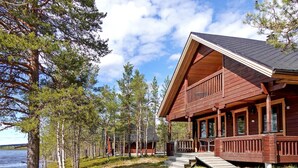 Une cabane en bois dotée d’un balcon, située au bord d’un lac, entourée d’arbres.