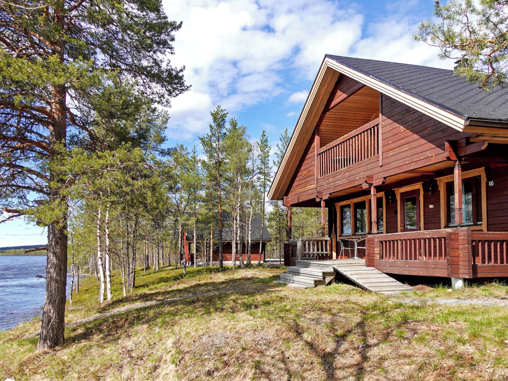 Puuinen mökki, jossa on kuisti, ja se sijaitsee järven rannalla puiden ympäröimänä.