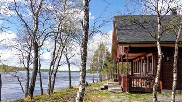 A cabin with a wooden deck overlooking a lake, surrounded by birch trees.