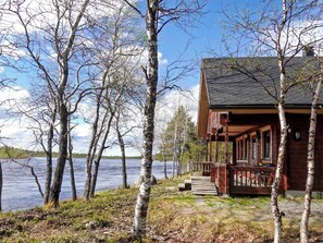 Une cabane dotée d’une terrasse en bois donnant sur un lac, entourée de bouleaux.
