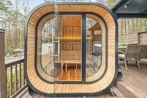 Eine runde Holzkonstruktion mit Glastür, einer Sitzbank im Inneren und einer umlaufenden Holzterrasse.