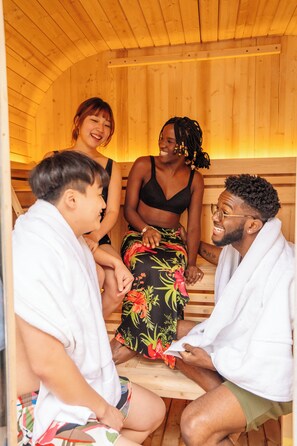 Eine Holzsauna mit vier Personen, die auf Bänken sitzen und sich unterhalten.