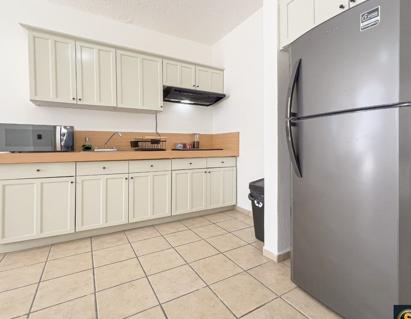 A kitchen with white cabinets, a stainless steel refrigerator, a microwave, and a sink.
