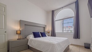 A bedroom with a bed, nightstands, a window with curtains, and a view of the outside. - Balandra Housing 2BR home downtown LPZ walk everywhere (La Paz)