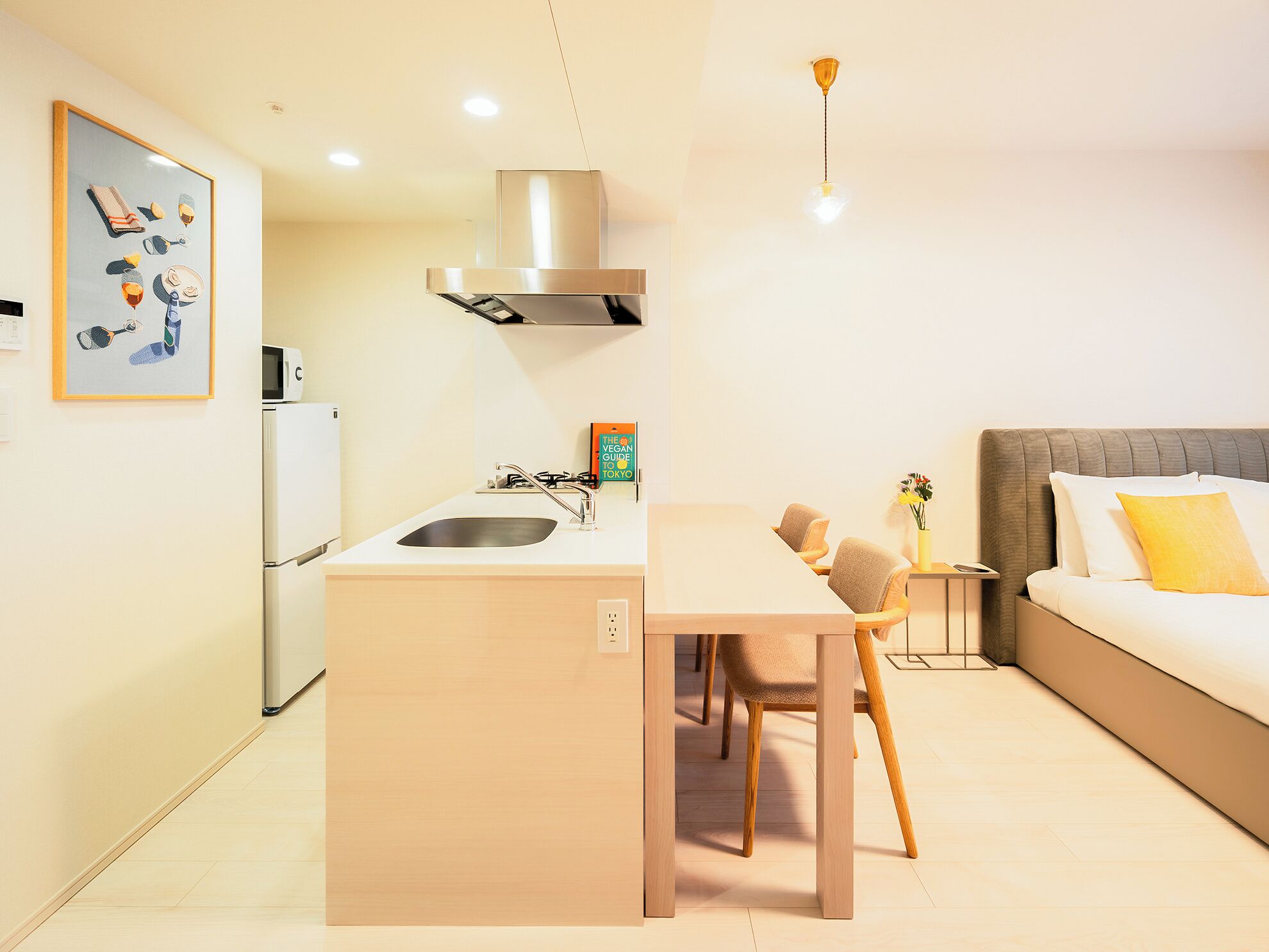 A modern kitchen with a central island, a dining area with chairs, a sofa, and a small table with a vase.