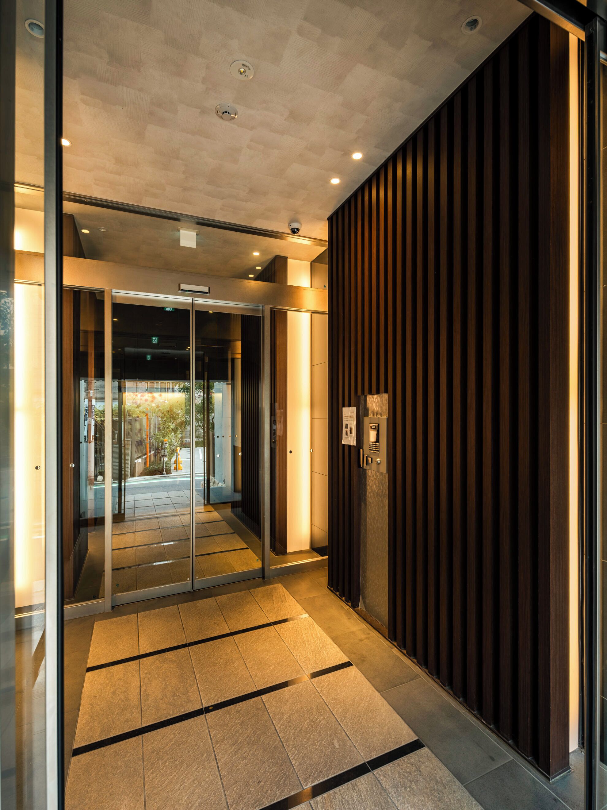 A modern interior with a glass entrance, a wooden wall, and a tiled floor.