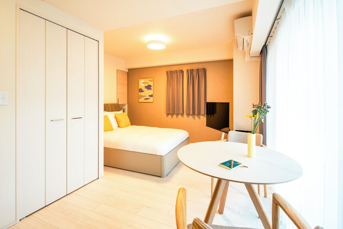 A hotel room with a bed, a round dining table, a chair, a TV, and a window with curtains.