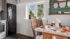 Uma cozinha com geladeira moderna, mesa de jantar posta para o chá e janela com vista para o verde.