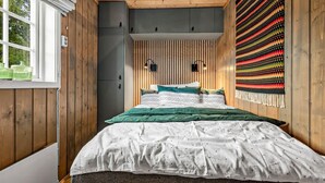 Quarto com parede de ripas de madeira, cama com roupa de cama verde e branca, e uma tapeçaria colorida na parede.