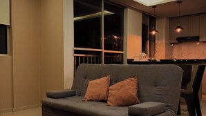 Ein modernes Wohnzimmer mit einem grauen Sofa, zwei braunen Kissen und einem gemusterten Teppich.