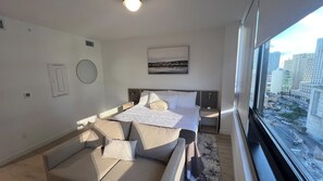 A modern bedroom with a bed, a sofa, a window with a city view, and a wall-mounted artwork. - New Studio Downtown Miami Bay View Rooftop Pool. (Miami)