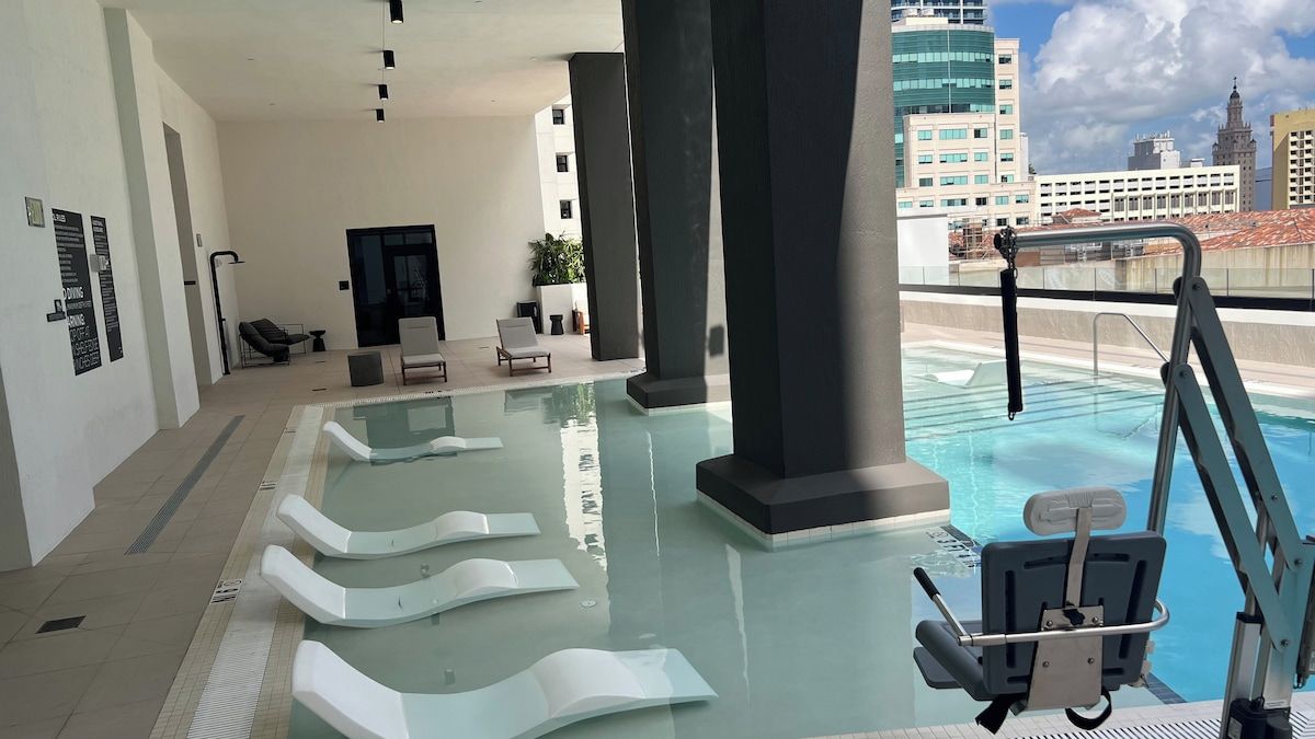 An indoor swimming pool with clear water, a diving board, and lounge chairs.