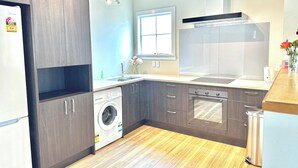 Une cuisine moderne avec des meubles en bois foncé, un lave-linge encastré, un évier en acier inoxydable et une grande fenêtre.